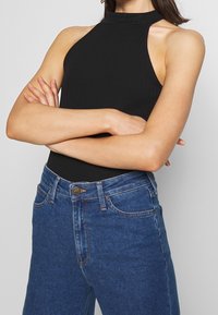 Czarny prążkowany top na halter z dekoltem po szyi, zestawiony z wysokim stanem niebieskich dżinsów z denimu, posiadających guzik Lee i klasyczny pięciopocketowy design.