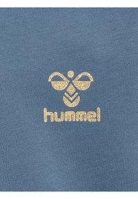 Světle modrá tkanina s texturovaným povrchem má zlatý design loga připomínajícího včelu nad slovem "hummel" ve stejné zlaté barvě.