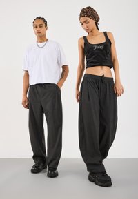 To personer iført løse mørkegrå bukser; den ene i en hvid oversized T-shirt og sorte sko, den anden i en sort crop top og leopardhovedbeklædning.