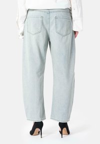 Lys blå denimjeans med en avslappet passform, med to baklommer og rå kant. Brukt med svarte høye hæler.
