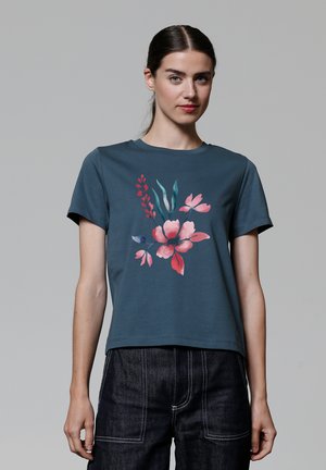 T-shirt à manches courtes teal avec un imprimé floral présentant des accents roses et verts. Encolure ronde et coupe droite.