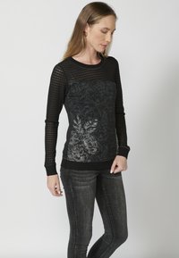 Pull noir avec des manches en maille longues, motif floral sur le corps, poignets et ourlet côtelés, avec des accents gris sur fond noir.