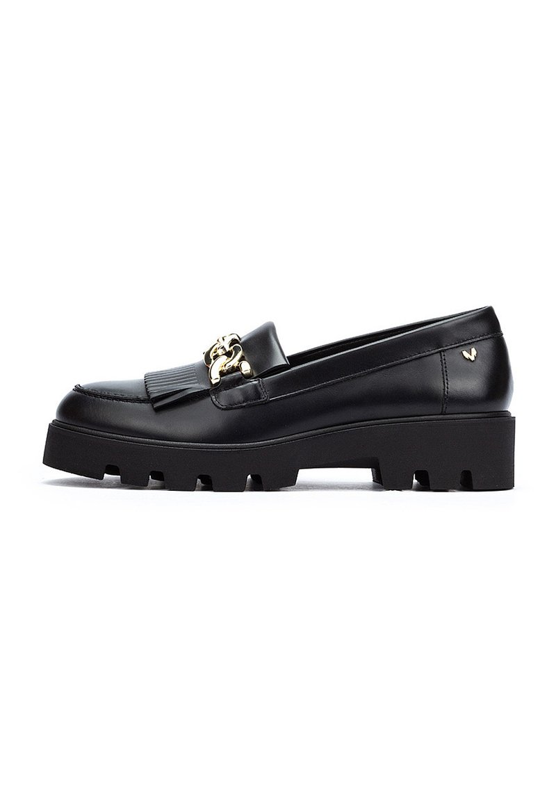 Mocasines de cuero negro con una suela gruesa y texturizada, que presentan un acento de hardware dorado y un detalle de diseño plisado en la parte superior.