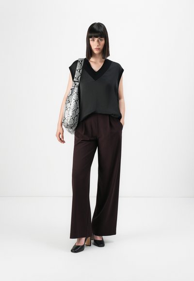 Top noir sans manches avec un décolleté en V, associé à un pantalon large marron. Un sac à main texturé au motif serpent et des talons noirs complètent le look.