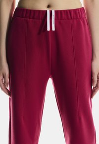 Punased trennipüksid elastse vööriga ja valgete nööridega. Omab küljetaskuid ning sujuvat, tekstuurset kangast viimistlust.