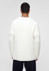 Weißer, kabelgestrickter Pullover mit strukturierter Oberfläche. Bietet eine lockere Passform und einen gerippten Saum. Die Rückansicht zeigt einen Rundhalsausschnitt und lange Ärmel.