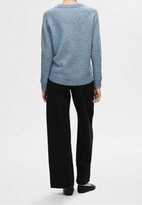 Vaaleansininen neulepaita pyöreällä pääntiellä ja resorireunuksella, yhdistettynä mustiin leveälahkeisiin housuihin ja mustiin tasapohjaisiin kenkiin.