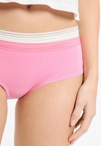 Różowe bawełniane majtki typu hipster z teksturowaną białą i szarą elastyczną tasiemką w pasie. Materiał jest gładki, o dopasowanym kroju.