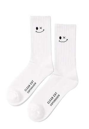 Calzini bianchi a costine, a girocollo, con volti sorridenti strizzanti un occhio ricamati in nero vicino alla parte superiore e la scritta "CLEAN CUT COPENHAGEN" stampata sulla zona del piede.