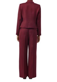 Bordowy garnitur składający się z dopasowanej marynarki z klapami oraz spodni o szerokich nogawkach, wykonany z gładkiego materiału o matowym wykończeniu.