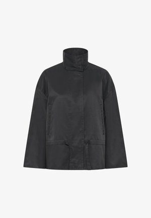 Must kergest ja siledast kangast jakk, millel on kõrge krae, kaks esimest taskut ja sirge lõige väheste õmblustega.