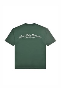 Camiseta verde de manga corta con texto en escritura blanca "Pas Dé Monaco" y un texto más pequeño "Deo Juvante" impreso en la parte superior de la espalda.