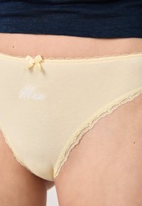 Culottes en coton jaunes avec des détails en dentelle, présentant une broderie "Muse" et un petit nœud sur la taille.