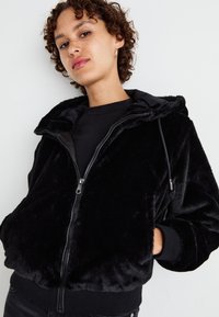 Zwarte ritssluiting hoodie van plush stof, met een capuchon, voorzakken en ribbing bij de mouwen. Glad, zacht textuur met een ontspannen pasvorm.