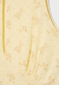 Tissu jaune sans manches avec un motif floral et de points orange clair subtil, avec un détail de couture froncée.