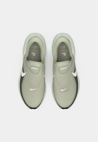 Ανοιχτόγρινα αθλητικά παπούτσια με υφή στο επάνω μέρος, λευκό λογότυπο Nike, πράσινες λεπτομέρειες στο πλάι και λείο, στρογγυλεμένο πάτο. Απλός σχεδιασμός.