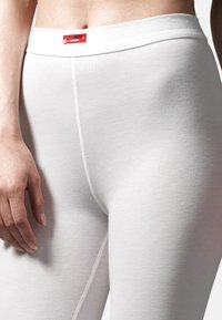 Leggings termici bianchi con una superficie liscia, vita elastica e un piccolo etichetta rossa in vita. Focalizzati su comfort e copertura.