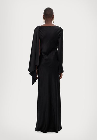 Un vestido negro de manga larga en tejido suave con un detalle de capa fluida. Presenta un escote cuadrado y una silueta ajustada.