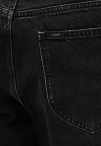 Κοντινό πλάνο από την πίσω τσέπη μαύρου τζιν με μια μικρή μαύρη ετικέτα με την επιγραφή "Lee" ραμμένη στην πάνω άκρη.