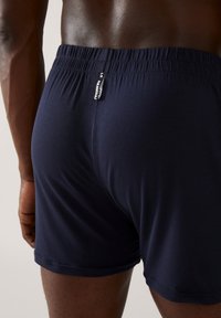 Boxers bleu marine en tissu doux avec une taille élastique et de petits détails de tag. Le design est ajusté avec une texture lisse.
