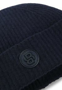 Berretto a maglia blu navy realizzato in morbida lana, con una texture a coste e un'etichetta rotonda nera con un design in rilievo.