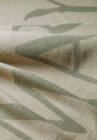 Tissu textile avec une base beige douce ornée de motifs géométriques verts. La texture semble lisse, avec de subtiles variations de couleur.