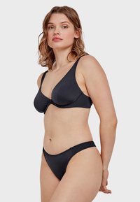 Completo bikini nero con bralette a triangolo dotata di coppe sagomate e spalline regolabili, abbinato a un pantaloncino a vita bassa. Tessuto liscio e stretch.