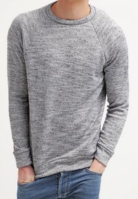 Sudadera gris de manga larga con un patrón texturizado, cuello redondo y mangas raglán, combinada con unos vaqueros de mezclilla azul.