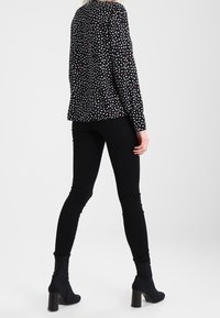 Maglietta nera a maniche lunghe con motivo triangolare bianco e rosso, abbinata a jeans skinny neri e stivaletti, vista da dietro.