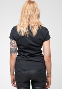 Black short-sleeve t-shirt made of cotton, slightly fitted design, displayed from the back, complemented by a tattoo on the left arm.