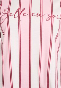 Striped t-shirt in light pink and white, featuring thin red stripes. Text "Belle en soi" in red across the front. Soft cotton material.