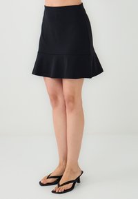 Zwarte flared mini-jurk gemaakt van zachte stof, met een aansluitende tailleband en een gerimpelde zoom. Gecombineerd met zwarte slippers.