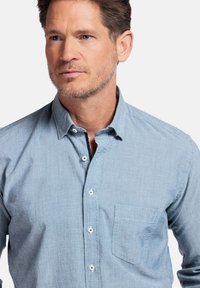 Chemise bouton-up bleu clair en tissu texturé, dotée d'une seule poche sur la poitrine et de boutons blancs contrastants.