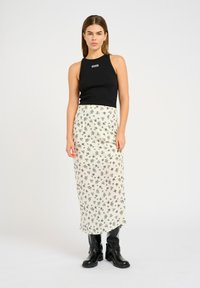 Top corto senza maniche nero con logo, abbinato a una maxi gonna bianca con motivo floreale e stivali neri al ginocchio con tacco. Design semplice e moderno.