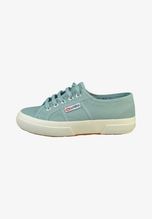 Zapatilla baja de lona azul claro con suela y cordones de goma blanca, con una pequeña etiqueta de tela con la marca "Superga" en el lado.