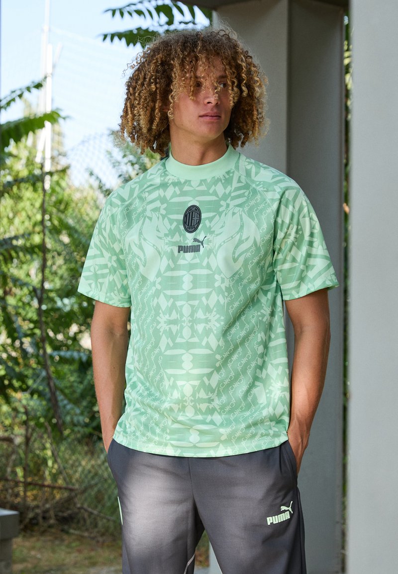 Camisa atlética de color verde claro con patrones geométricos, de manga corta y cuello redondo. Logotipo negro de Puma en el pecho y emblema del club en el centro.
