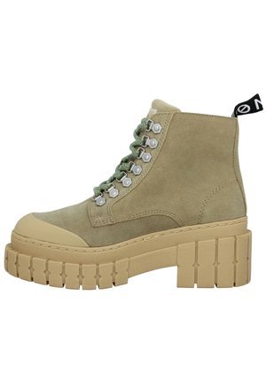 Bottine beige en daim avec semelle crantée épaisse, lacets verts, œillets métalliques, bout renforcé et languette noire au talon.