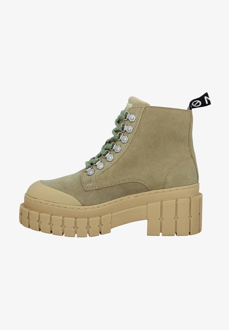 Bottine beige en daim avec semelle crantée épaisse, lacets verts, œillets métalliques, bout renforcé et languette noire au talon.