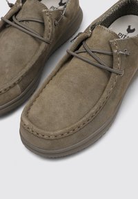 Scarpe slip-on in suede marrone con punta arrotondata, cuciture a contrasto e suola flessibile. Presentano un dettaglio di lacci decorativo sulla parte superiore.