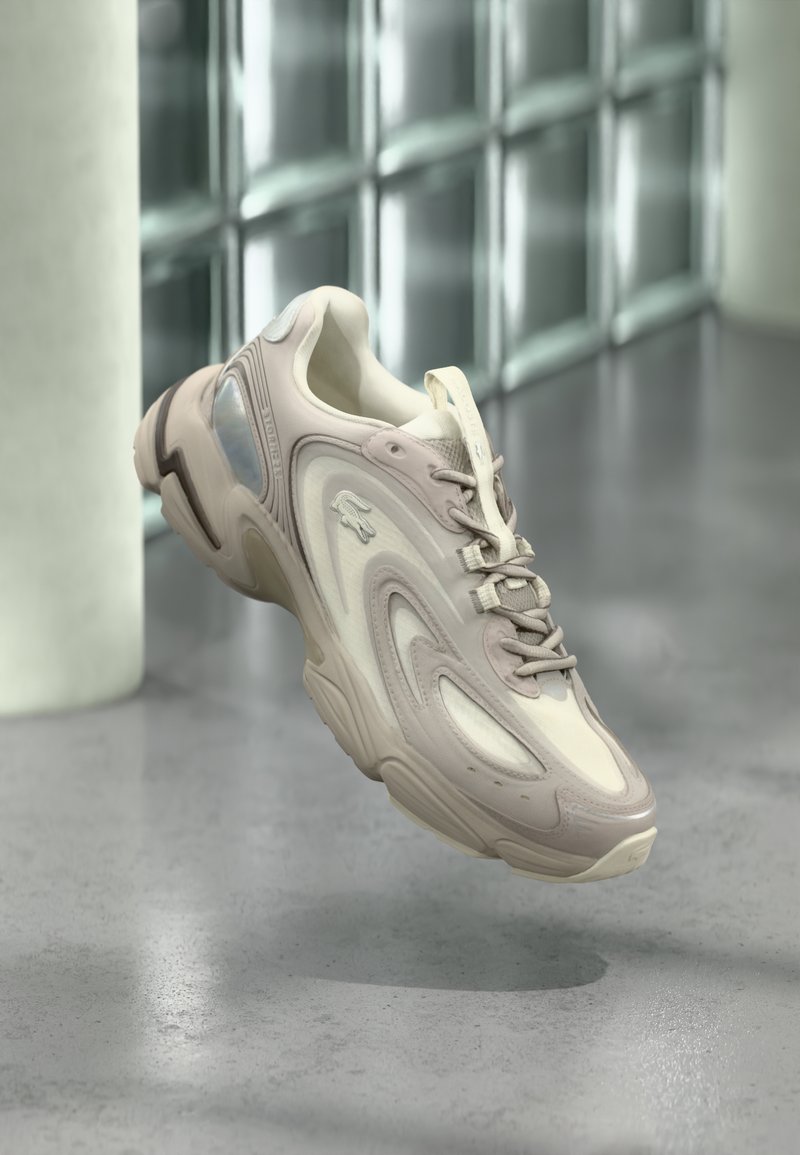 Baskets beige clair dotées d'un design élégant avec des superpositions texturées, une semelle rembourrée et une section translucide sur le côté.