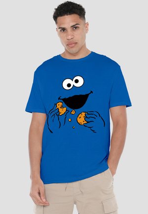 Blaues Baumwoll-T-Shirt mit einem grafischen Druck eines Charakters mit großen Augen und Mund, der Kekse hält, bei denen die Brösel sichtbar sind.