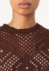 Top marrone lavorato a maglia con un motivo di tessitura aperta decorato da dettagli luccicanti. Il collo è a coste, mettendo in risalto un design testurizzato.