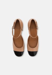 Balerini din piele lacuită bej cu vârf negru, dotate cu brățară la gleznă și design cu vârf rotund. Textură netedă, stil minimalist.
