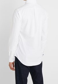 Witte blouse met lange mouwen, voorzien van een button-down kraag, rugstuk en afgeronde zoom. Gemaakt van glad katoen met manchetknopen.