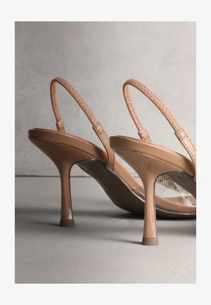Paire de chaussures à talons hauts couleur camel avec fines brides tissées et talons pointus sur une surface grise, sur un fond neutre.