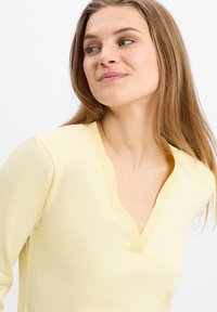 Light yellow V-neck top with smooth texture and fitted design; features a soft neckline and long sleeves.