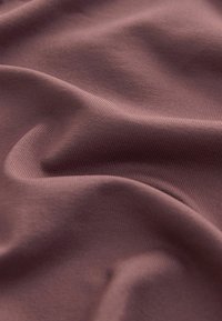 Tissu doux et froissé de couleur mauve sourde avec une texture fine côtelée et de légers plis créant une surface lisse et fluide.
