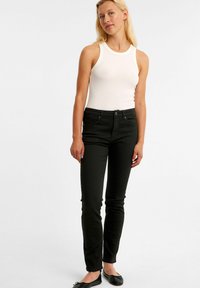 Svart högmidjade jeans med slim fit, tillverkade av denim. Återfinns tillsammans med en vit ribbad tanktopp och svarta platta skor. Inga synliga mönster.