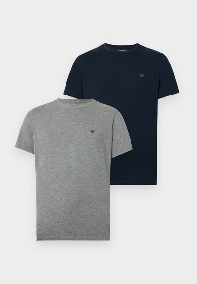 Δύο μονόχρωμα μπλουζάκια με στρογγυλή λαιμόκοψη, ένα γκρι και ένα ναυτικού μπλε, καθένα με μικρό λογότυπο στο αριστερό στήθος.