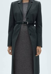 Blazer ajusté gris foncé avec un col cranté, design à un bouton, deux boutons, et une ceinture noire, associé à une robe grise cintrée.